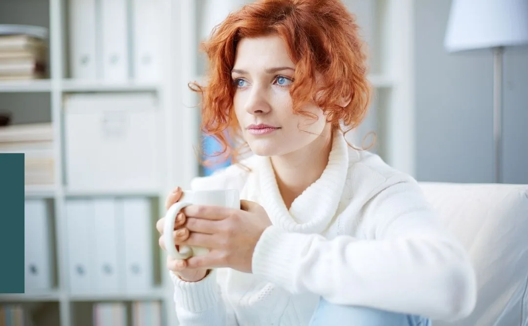 Une femme tient une tasse entre ses mains et regarde par la fenêtre